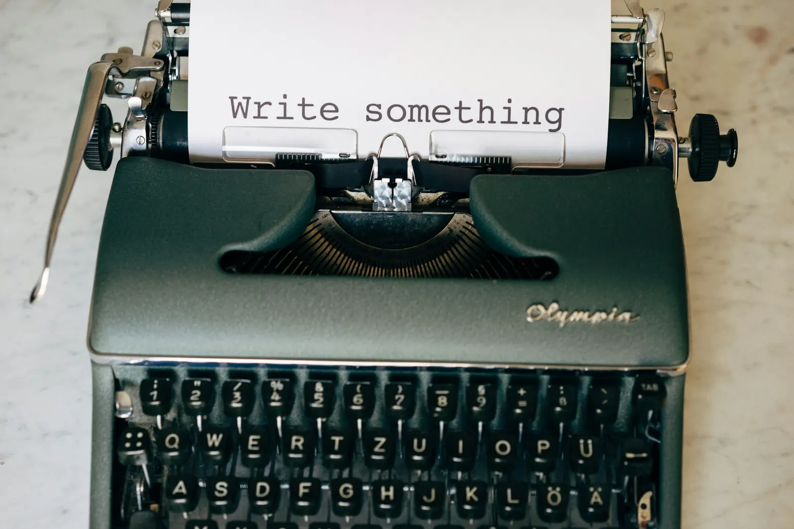 An Olympia typewriter on a marble surface with a sheet of paper reading Write something