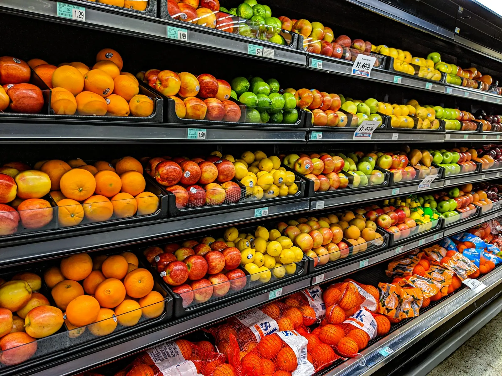 Supermarket shelves stacked with oranges, apples, lemons, and limes side by side