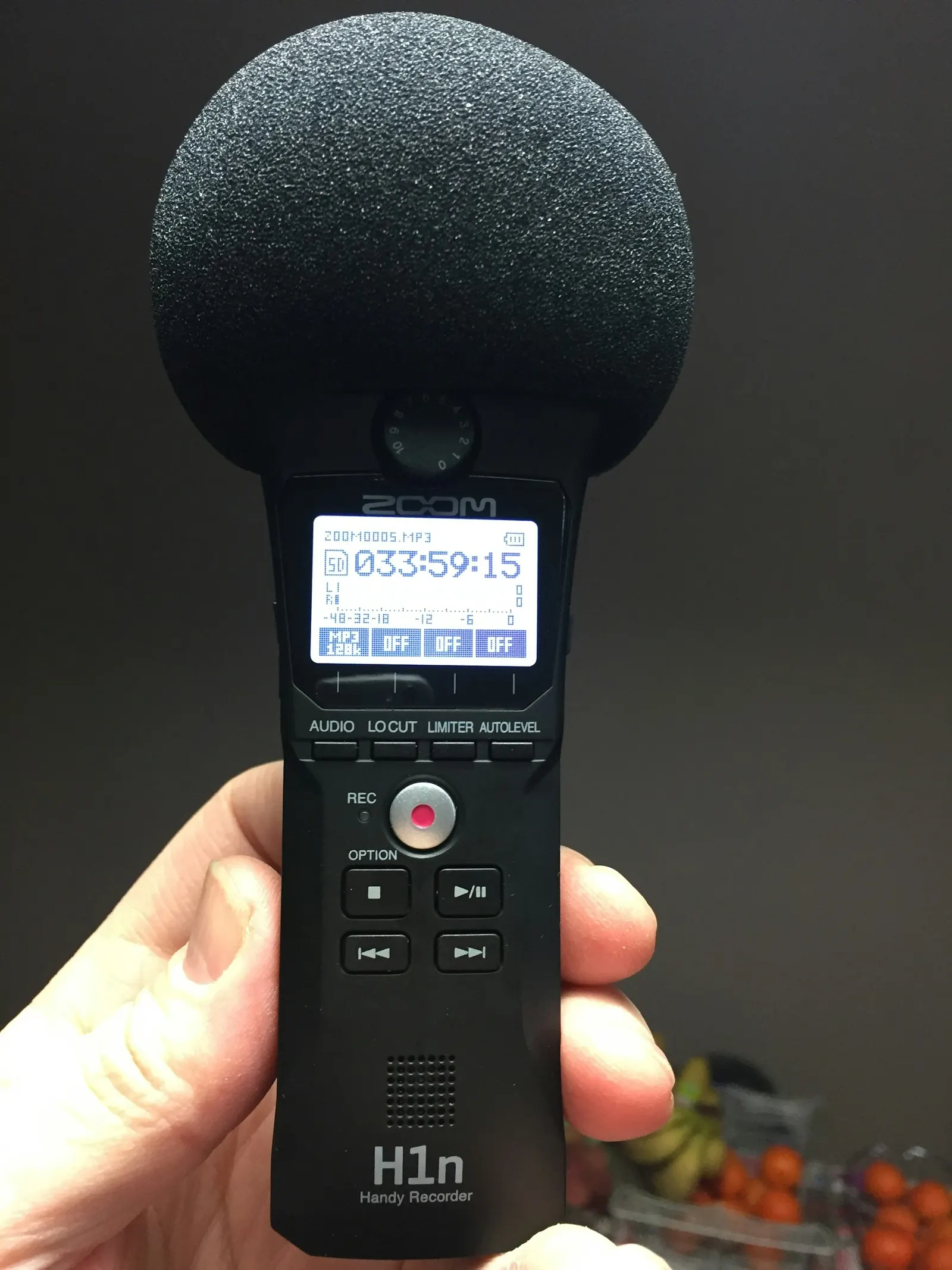 Hand holding a digital audio recorder with a foam windscreen, ready to record an interview