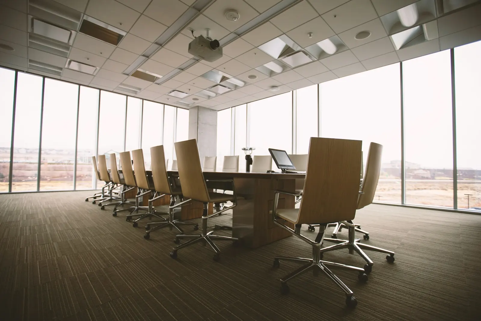 An empty boardroom with a long wooden table, office chairs, and floor-to-ceiling windows