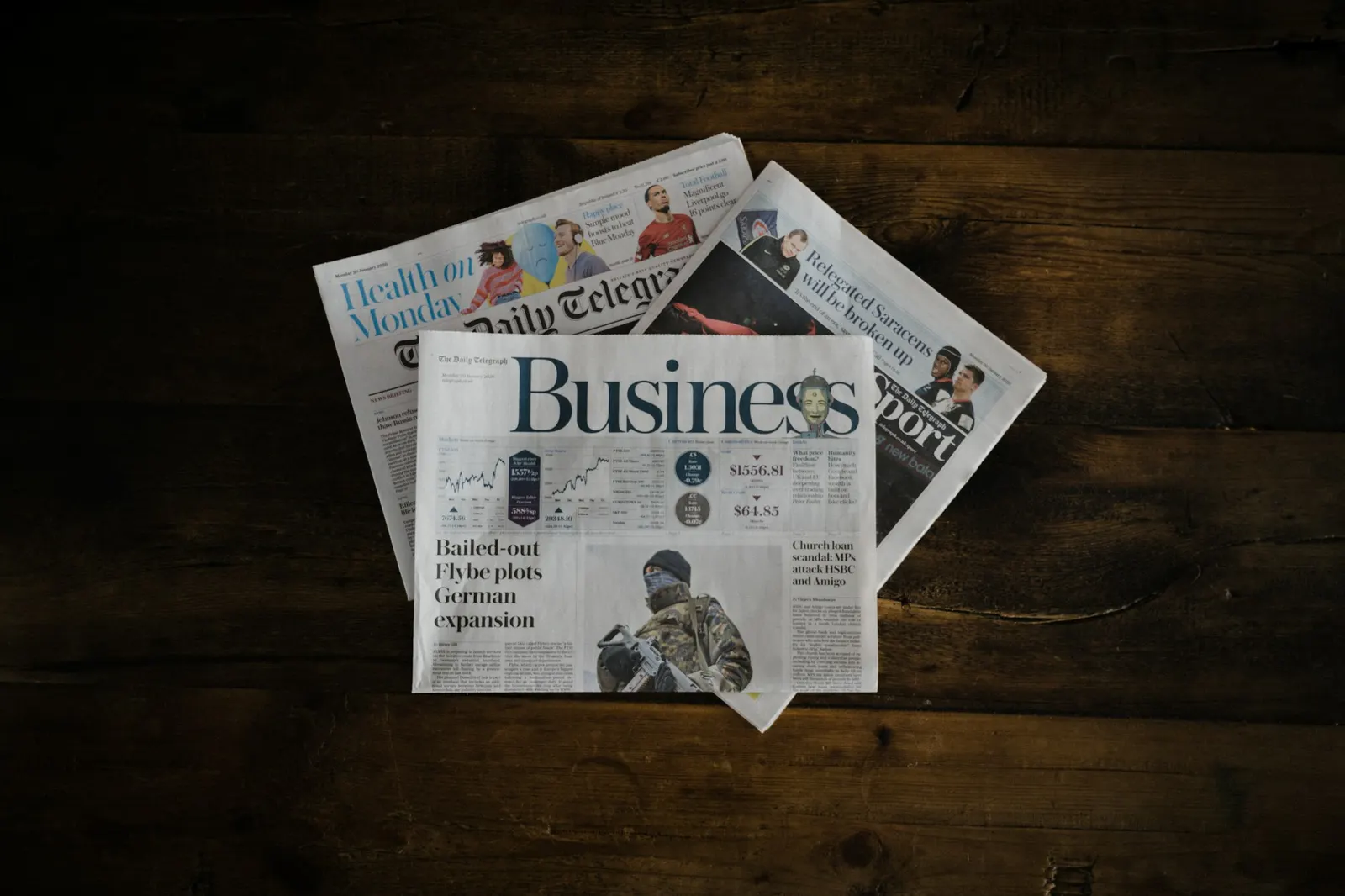 A stack of newspapers, with the business section on top, on a wooden table