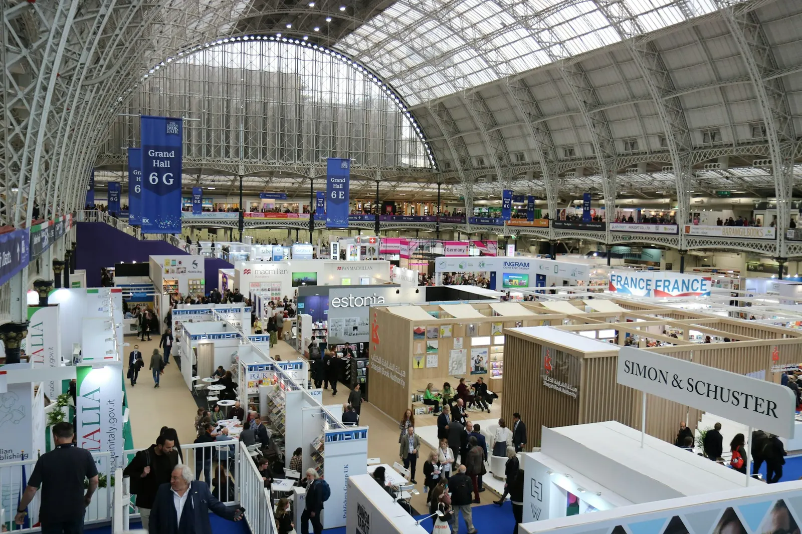 A busy trade show exhibition hall with publisher booths and attendees seen from a balcony