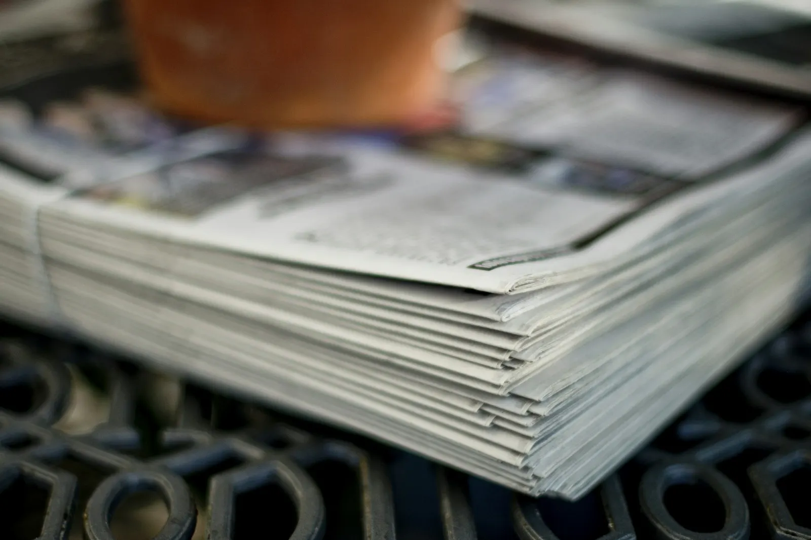A thick stack of folded newspapers bound together on a metal grate, with a blurred figure behind