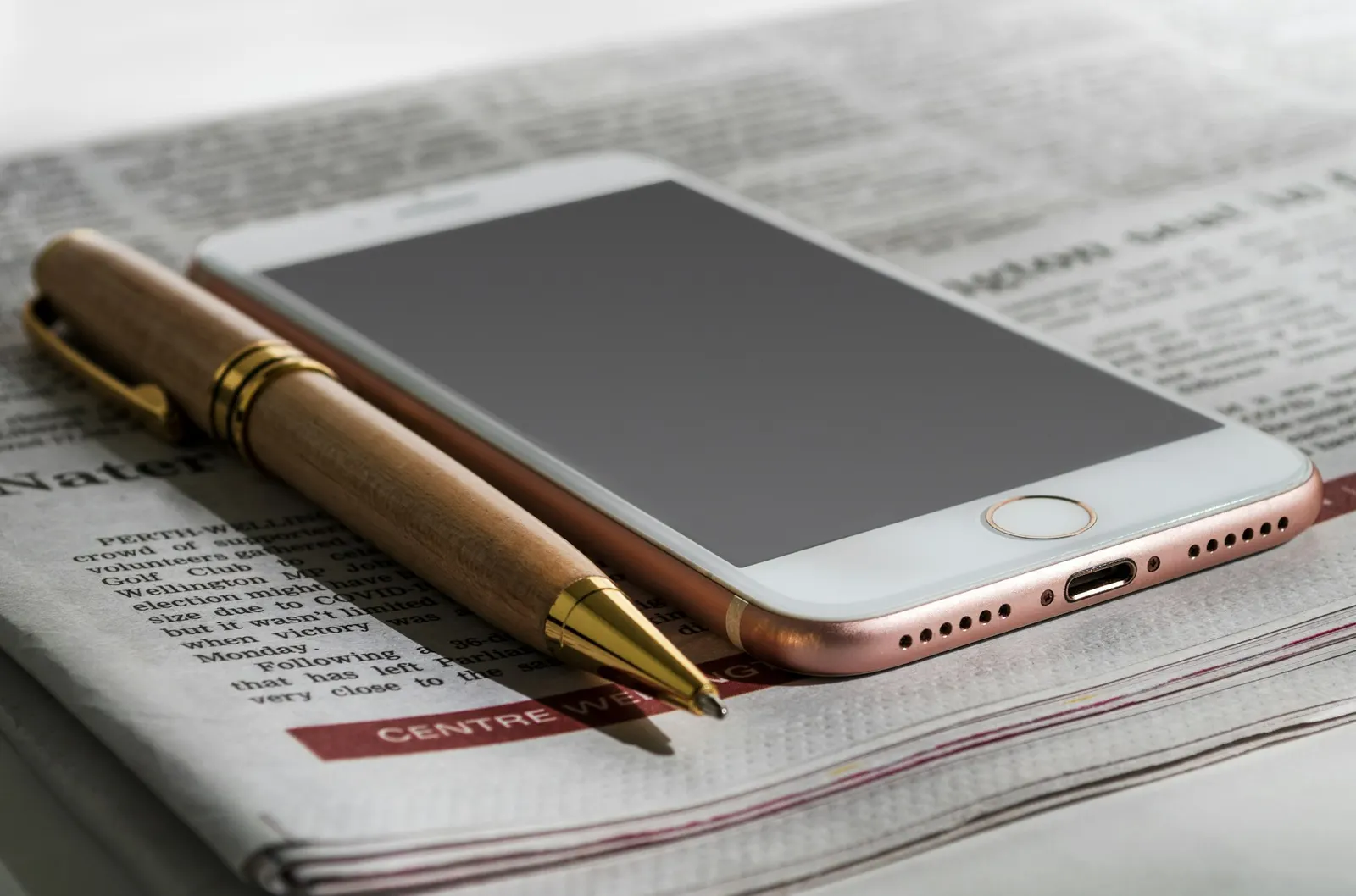 A smartphone and a wooden pen resting on a folded newspaper