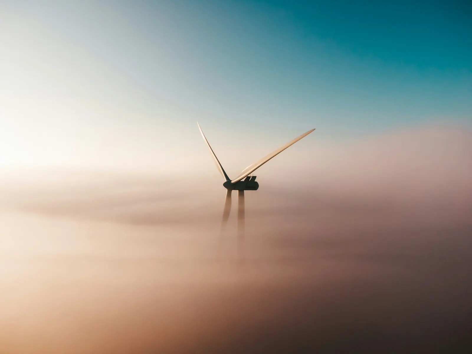 A single wind turbine rising out of morning fog at sunrise