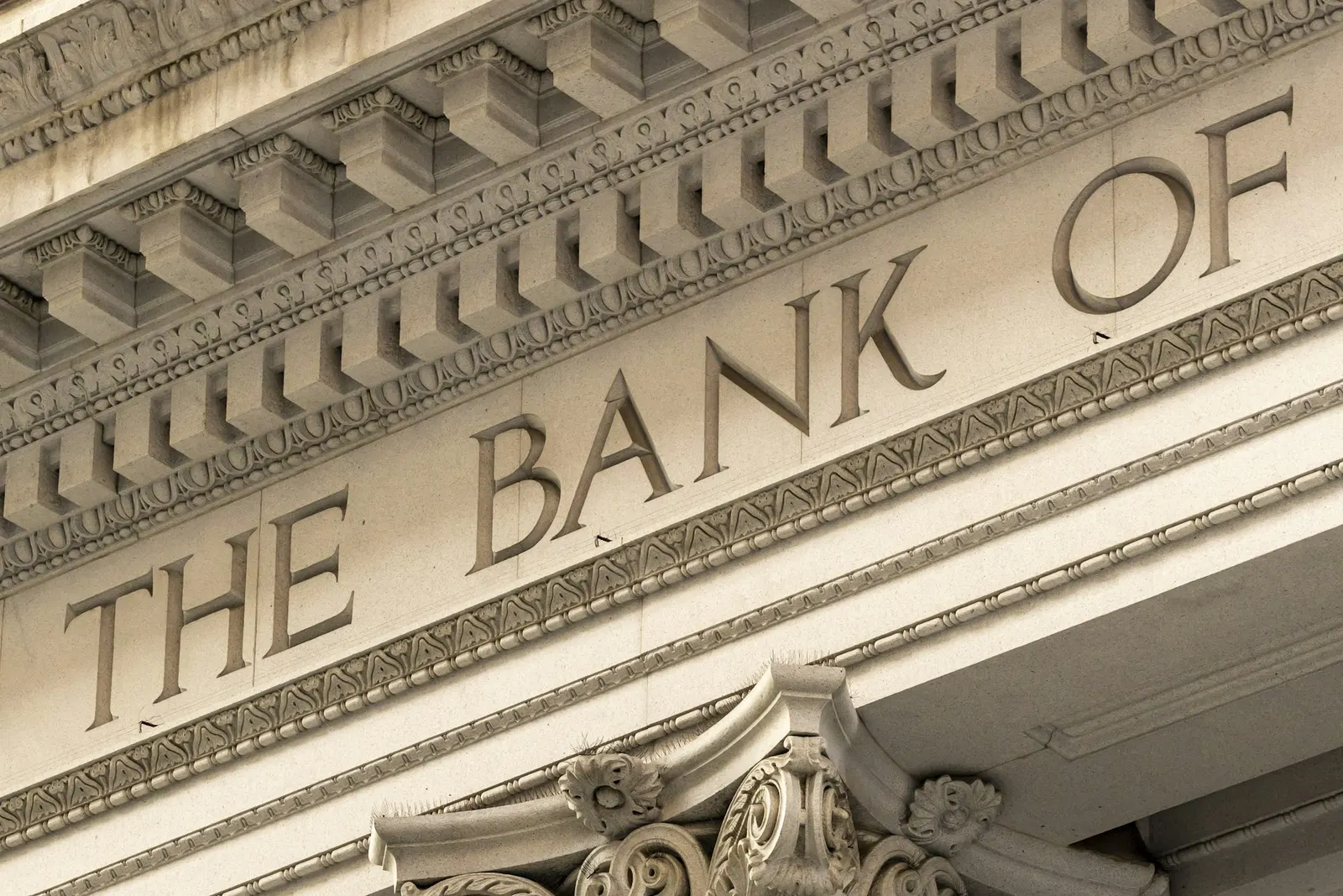 The carved facade of a classical bank building with the words The Bank Of above ornate columns