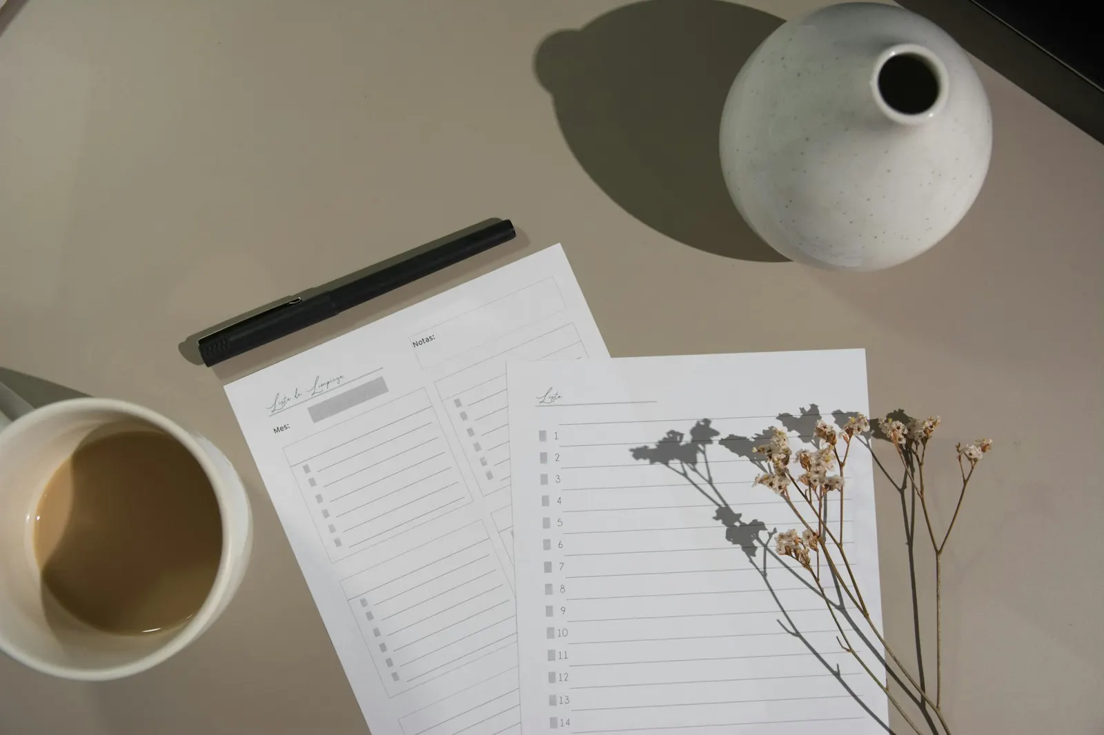 Printed planning checklists and a pen on a desk beside a cup of coffee and a ceramic vase