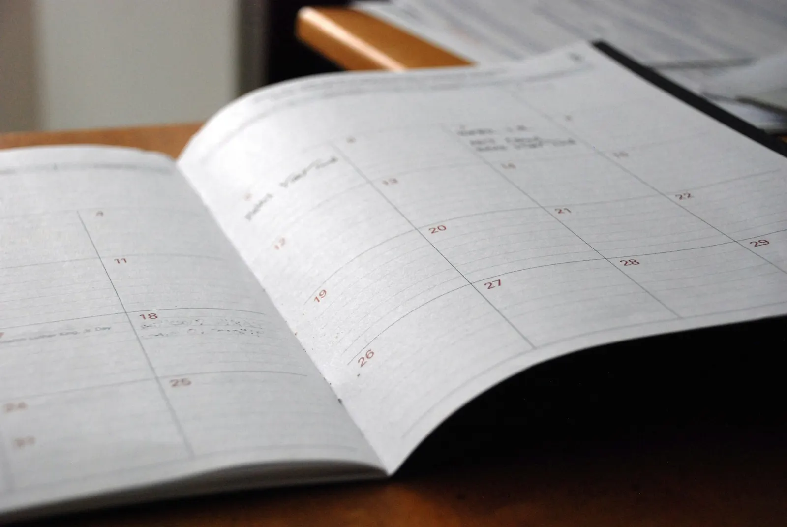 An open monthly planner on a wooden desk with handwritten notes on several dates