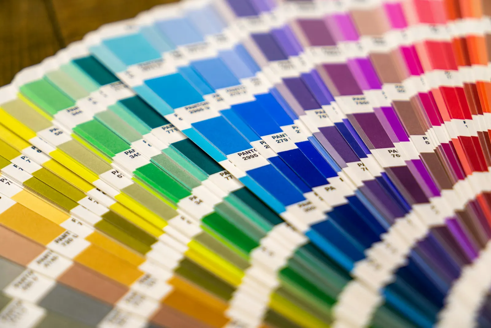 A fan deck of printed color swatches arranged in a spectrum from yellow and green through blue, purple, and red