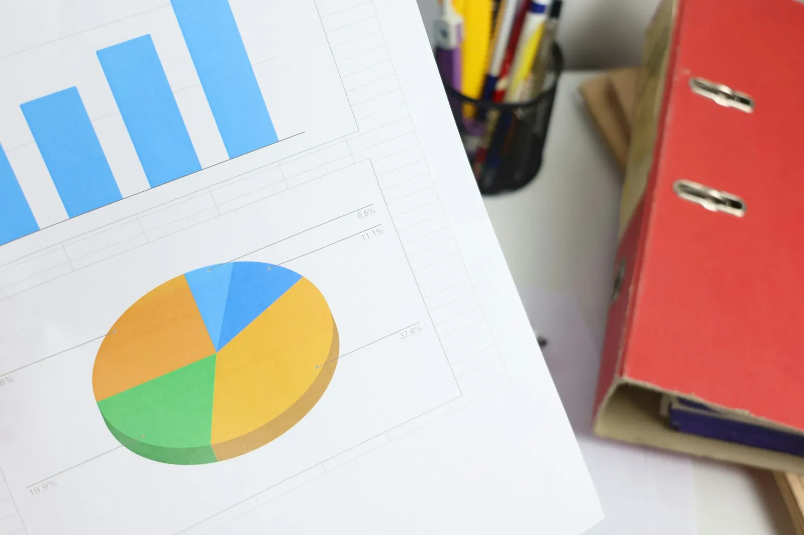Printed bar and pie charts on a desk next to a red binder, the raw material of a year-end data story