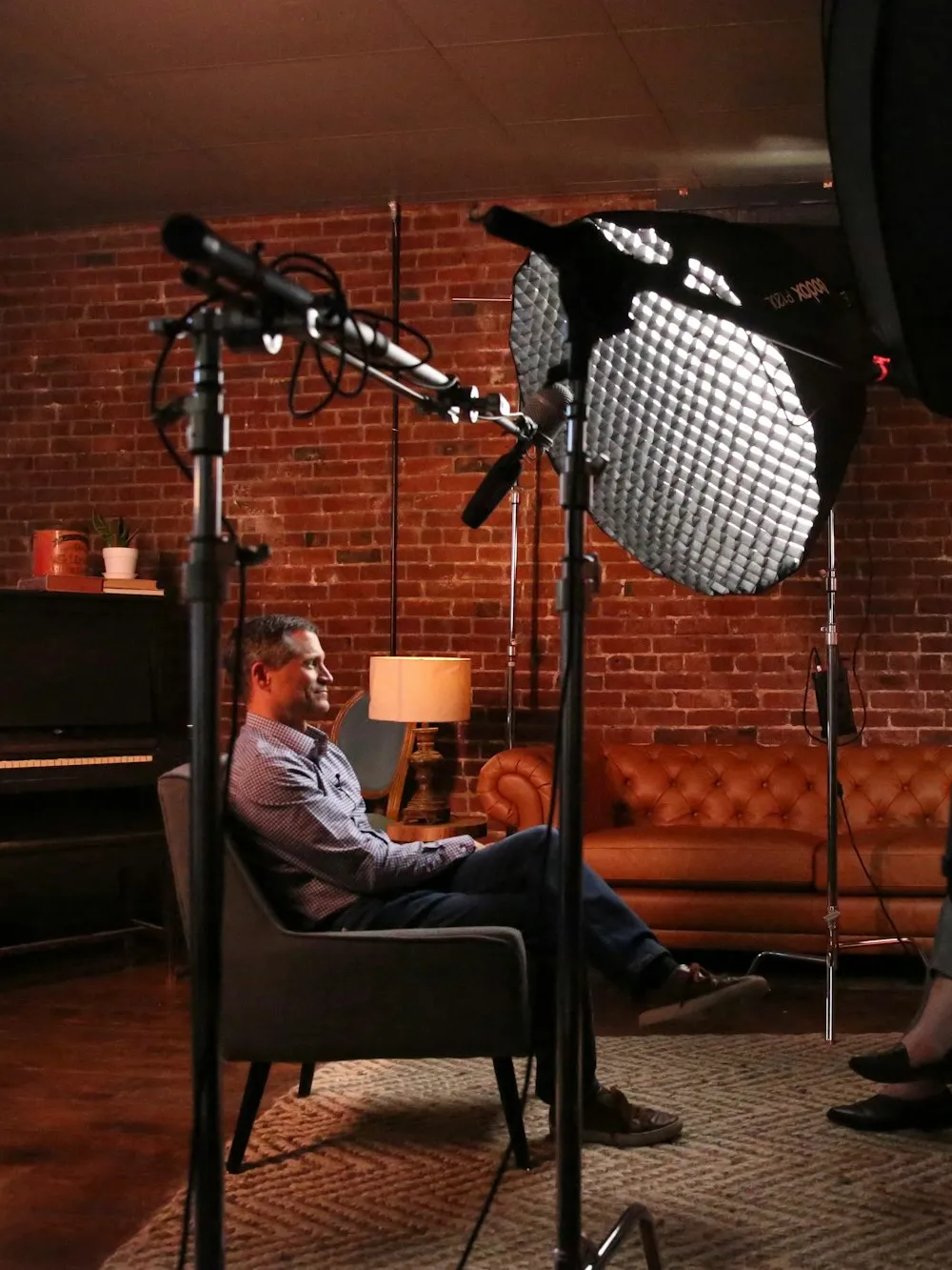 An executive seated for a studio broadcast interview, lit by softboxes with a boom microphone overhead